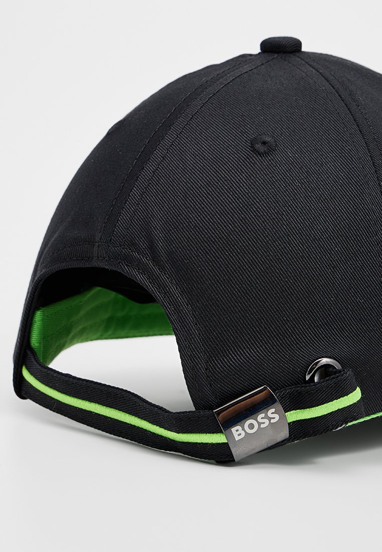 Casquette de baseball noire avec doublure intérieure verte, présentant un design structuré, des rayures accentuées et un logo en métal sur la sangle ajustable.