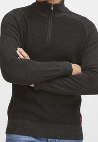 Pull gris foncé à fermeture éclair, tricot texturé, col montant et poignets côtelés. Comprend une petite étiquette logo à l'ourlet.