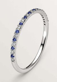 Anillo de plata con una banda delgada adornada con piedras azules y transparentes alternadas, creando un efecto brillante. Acabado suave y pulido.