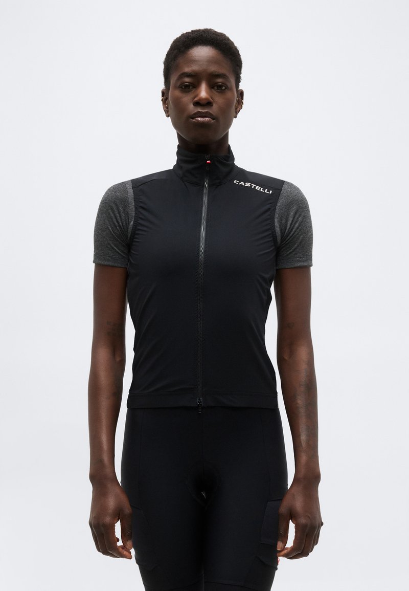 Vrouw draagt een zwart mouwloos fietsvest over een grijs T-shirt met korte mouwen, staand tegen een effen lichte achtergrond.