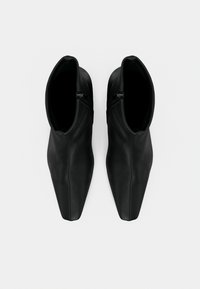 Ζευγάρι μαύρα δερμάτινα μποτάκια αστραγάλου με μυτερά δάχτυλα και πλευρικά φερμουάρ, βλέποντας από πάνω σε λευκό φόντο.