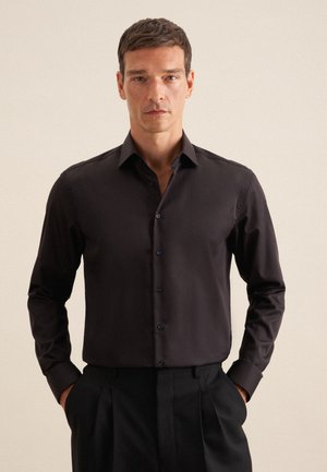 Schwarzes Langarmshirt aus glattem Material, mit einem klassischen Kragen und Knopfleiste, kombiniert mit schwarzen Hosen. Keine Muster sichtbar.