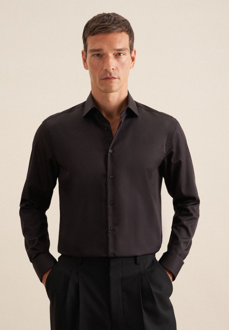 Camicia nera a maniche lunghe realizzata in tessuto morbido, con colletto classico e chiusura a bottoni, abbinata a pantaloni neri. Nessun motivo visibile.