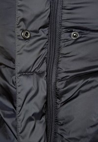 Svart puffjacka med en central dragkedja, tryckknappar och quiltad textur. Materialet verkar glansigt och vadderat.