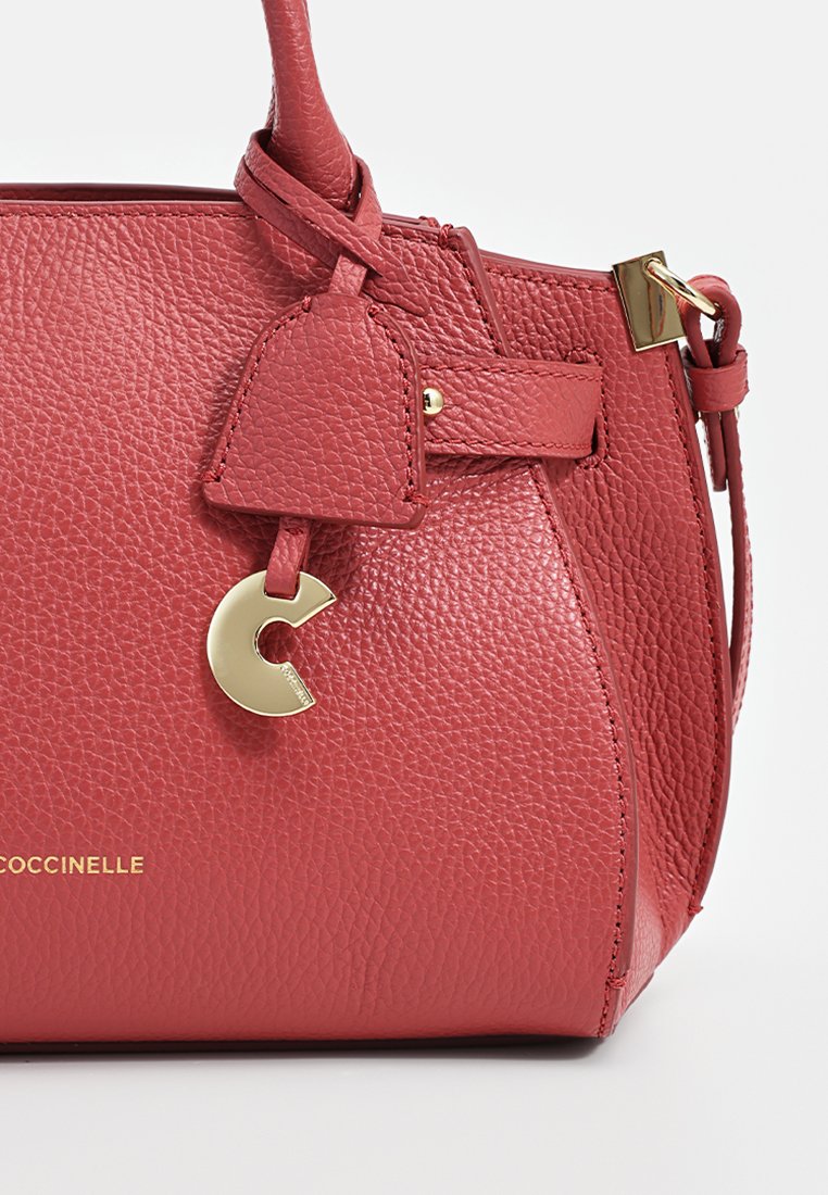 Borsa a mano in pelle rossa con finitura testurizzata, accessori in oro e un charm decorativo. Presenta un design strutturato e una maniglia corta.