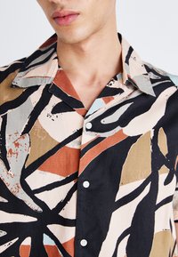 Chemise à manches courtes avec un motif abstrait en beige, noir, rouille et bleu clair ; fabriquée en tissu doux et respirant.