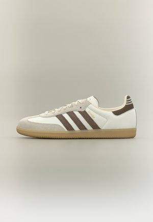 Scarpa Adidas Samba dal profilo basso in bianco e marrone con suola in gomma e strisce marroni, vista angolare a sinistra su sfondo neutro.