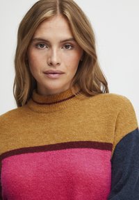 Pull en maille avec col haut ; présente des blocs de couleur or, rose et marine, un col côtelé et une texture douce.