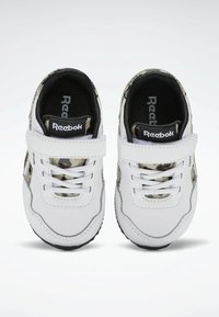 Baskets blanches avec des accents noirs et un motif camouflage sur les côtés. Équipées d'une bride à velcro et d'un laçage. Semelle en caoutchouc texturée.