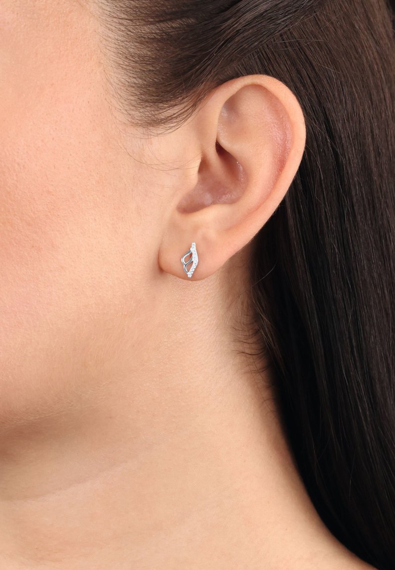 Silverörhänge med en böjd, öppen design och små inlagda stenar, bärs på vänster örsnibb av en person med mörkbrunt hår.