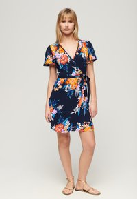 Abito avvolgente floreale in navy con motivi arancioni, rosa e bianchi. Maniche corte, vita legata e design alla lunghezza del ginocchio.