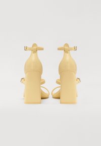 Yellow block-heeled sandals with ankle straps, smooth leather-like material, open toes, and minimalistic design.