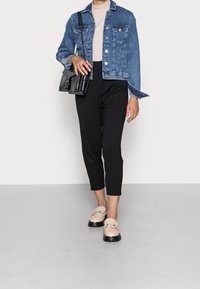 Veste en denim au design légèrement court, assortie à un pantalon noir ajusté et des mocassins beiges avec des semelles noires. Sac bandoulière noir.