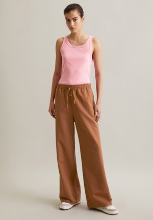 Rosa geripptes Tanktop kombiniert mit lockeren braunen Hosen und weißen Turnschuhen. Einfaches, lässiges Design mit Kordelzugbund und weitem Bein.