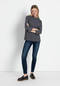 Grau gestreiftes Langarmshirt mit weitem Ausschnitt, kombiniert mit figurbetonten dunkelblauen Jeans und schwarzen Slippern. Glattes Material mit leichtem Glanz.