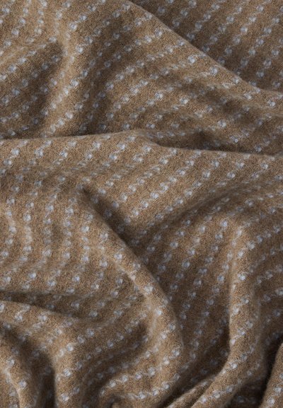 Tissu marron tissé avec une texture douce, décoré de motifs à pois blancs et de lignes ondulées, créant un design rythmique sur la surface.