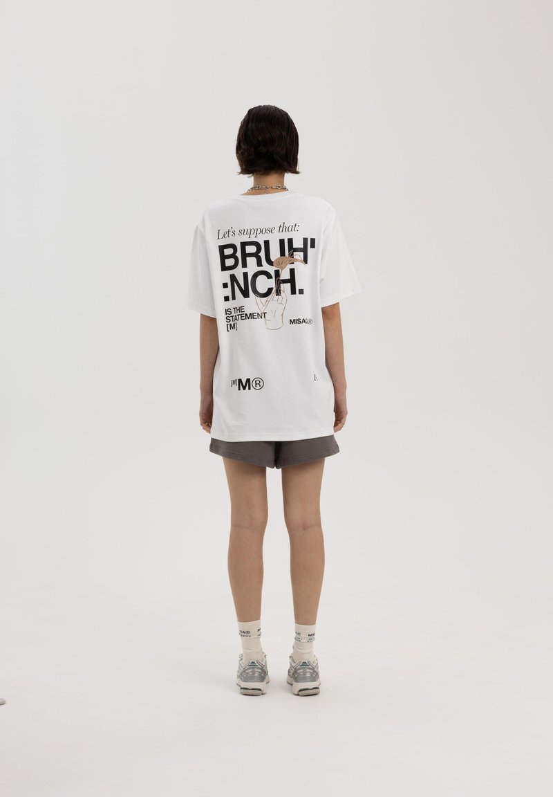 Witte oversized t-shirt met zwarte tekst en een afbeelding op de achterkant. Zachte katoenen stof, korte mouwen, casual ontwerp. Gepaarde met grijze shorts.