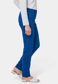 Blauwe, rekbare broek met een gladde textuur en een elastische tailleband, gecombineerd met open-toe witte sandalen met een lage hak.