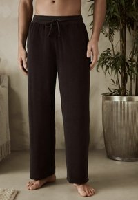 Pantalones de lounge de tejido de rizo negro y suave con cinturilla elástica y cordón. Presentan piernas rectas y un ajuste relajado.