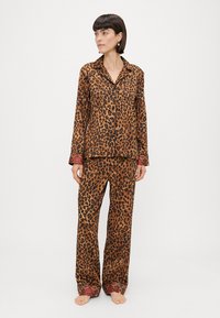 Pajama komplet s leopardjim vzorcem v mehkem materialu; dolgi rokavi s gumbom, usklajeni hlače z dekorativnim robom v rdeči barvi.