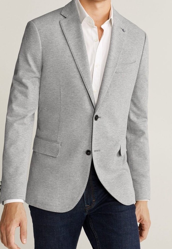 Grijze blazer van gestructureerde stof met een reverskraag, twee voorzakken en een enkele knoopsluiting, gedragen over een wit overhemd.