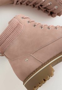 Botas de tobillo de imitación cuero rosa con un cuello de canalé, ojales metálicos y suela de goma texturizada con tacos pronunciados para mayor tracción.