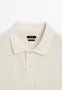 Polo en coton blanc cassé avec col pointu, deux boutons et étiquette de marque noire indiquant "Massimo Dutti" à l'intérieur du col.