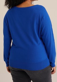 Blue sweater with a loose fit, long sleeves, and ribbed hem. Features a round neckline and textured knit fabric, paired with dark gray jeans.