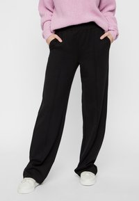 Black wide-leg trousers with a smooth texture, featuring side pockets and an elastic waistband, paired with white sneakers.