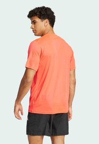 Camisa atlética de manga corta para hombre en tejido naranja brillante, con un sencillo cuello redondo y una textura ligera y suave.