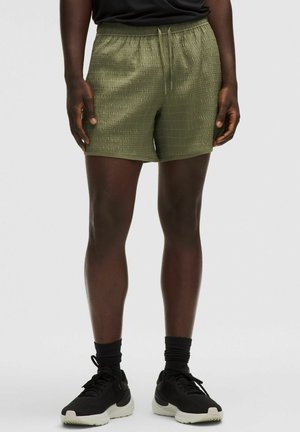 Olivegrüne Sportshorts mit einer strukturierten Oberfläche, elastischem Bund und Kordelzug. Kombiniert mit schwarzen Sportschuhen und Socken.