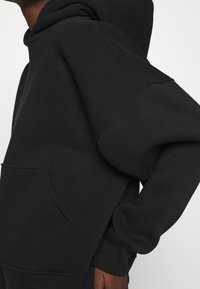 Czarna bluza z miękkiej bawełnianej mieszanki, z kieszenią kangurką, ściągaczami na rękawach i luźnym krojem z kapturem.