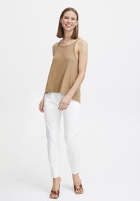 Tamna bez rukava majica s laganim, lepršavim dizajnom; uparena s bijelim slim fit hlačama i smeškim sandalama na petu. Jednostavan, minimalistički stil.