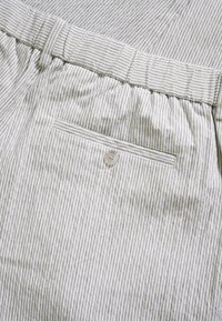 Tissu rayé en beige clair et olive avec une poche arrière boutonnée. Taille élastique avec un détail plissé, offrant une coupe décontractée.