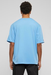 Šviesiai mėlyna trumpomis rankovėmis marškinėliai, pagaminti iš tekstūruoto audinio, su apykakle ir laisva forma, rodomi iš nugaros.