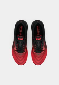 Punane ja mustad Reebok Nano XV treeningjalanõud mustade paeltega, vaadatuna ülevalt valgel taustal.