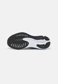 Curved black rubber outsole with wavy tread pattern and white accent, featuring cutouts and grooves for flexibility and grip.