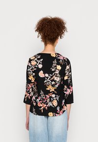 Blusa preta floral com mangas três quartos, apresentando padrões de flores multicoloridas e um decote redondo, feita de tecido macio.