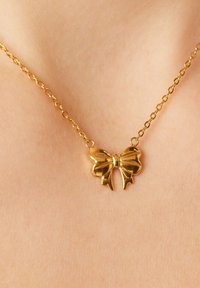 Gouden vlinderketting met een glanzende, gedetailleerde hanger bevestigd aan een delicate ketting, rustend op een lichte huidtint achtergrond.