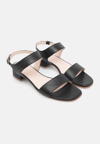 Zwarte leren sandalen met een lage vierkante hak, voorzien van twee brede banden over de voet en een enkelriem met een gesp. Platte zool.