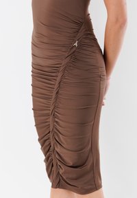 Vestito aderente marrone realizzato in tessuto elasticizzato, con arricciature laterali e un accento metallico decorativo. Tessuto liscio con orlo a lunghezza ginocchio.