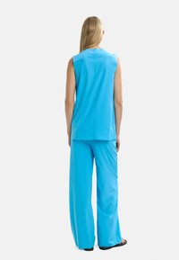 Dopasowany bezrękawnik i szerokie spodnie w jasnoniebieskim kolorze, z gładką fakturą i minimalistycznym wzornictwem, z detalem w postaci szwu na plecach.