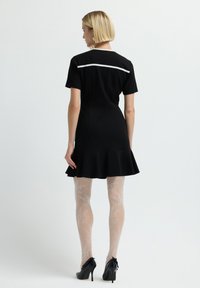Czarna sukienka z rozkloszowanym dołem, krótkimi rękawami i białym akcentem na plecach. Noszona z wzorzystymi jasnymi rajstopami i czarnymi wysokimi obcasami.