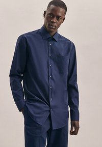 Camicia blu navy con bottoni in tessuto liscio, con colletto, maniche lunghe e taschino sul petto. Presenta un orlo dritto e chiusura frontale con bottoni.