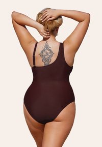 Bañador de una sola pieza marrón con una textura suave, que presenta tirantes anchos y un diseño de espalda baja, exhibiendo un tatuaje decorativo en la parte posterior.