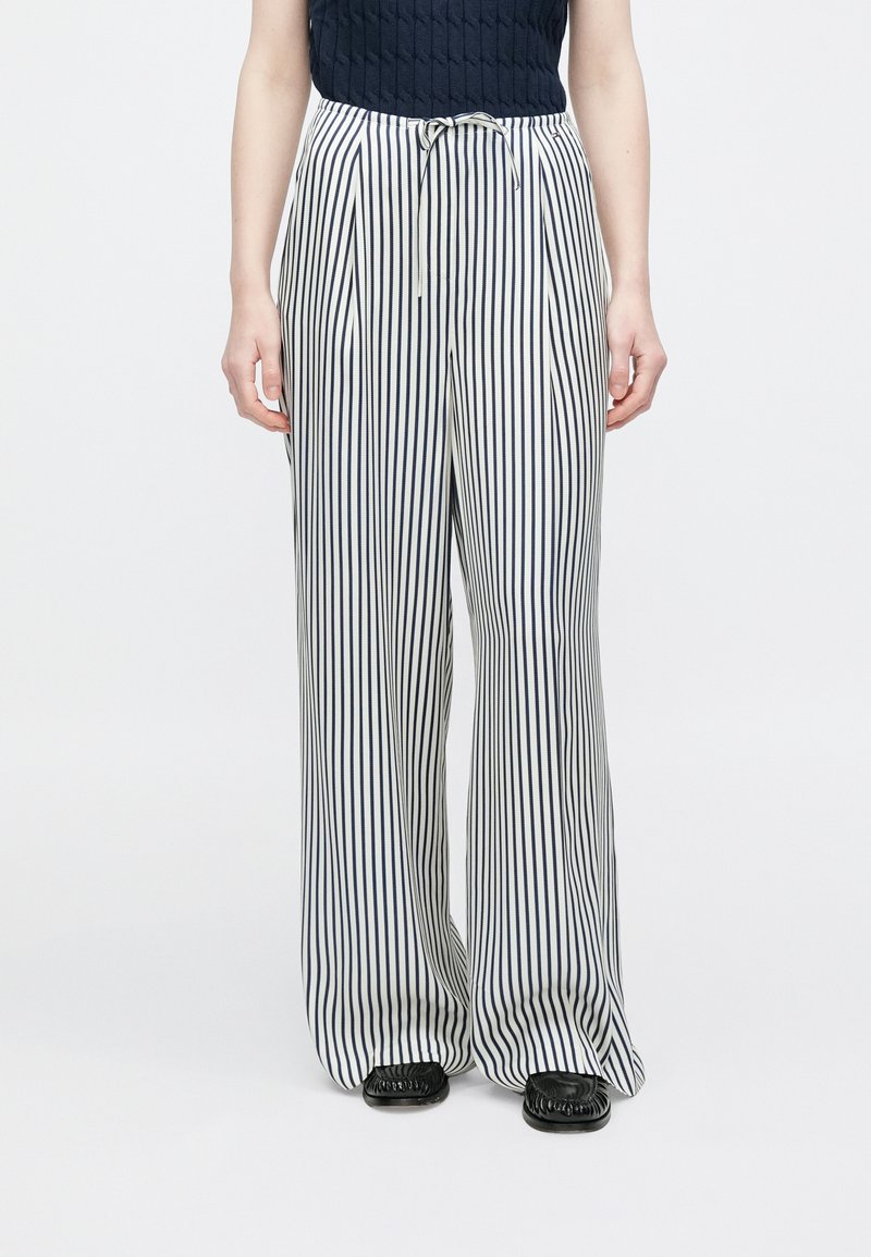 Hlače širokih nogavica s prugama u bijeloj i tamnoplavoj boji, s remenom za zatezanje u struku. Meki materijal s okomitim prugama za opušteni kroj.