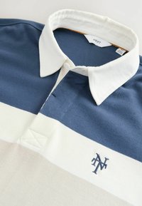 Navy, cream, and beige striped polo shirt made of cotton. Features a white collar, button placket, and embroidered ‘N’ logo on the chest.
