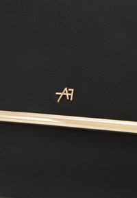 Czarna skórzana torba z złotymi metalowymi akcentami i logo. Gładka tekstura w eleganckim, prostokątnym kształcie. Minimalistyczny design.