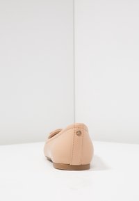 Ballerine nude in materiale sintetico liscio; presentano una punta arrotondata e un piccolo dettaglio triangolare in metallo sul tallone.