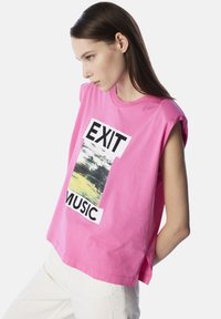 Roze katoenen t-shirt met korte mouwen, voorzien van een grafische print met de woorden "EXIT" en "MUSIC," met een landschapsontwerp in het midden.